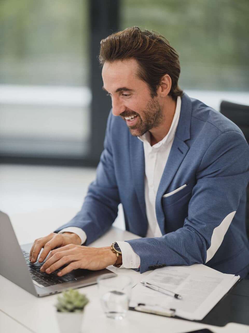 A professional smiling while working on a laptop in a bright office